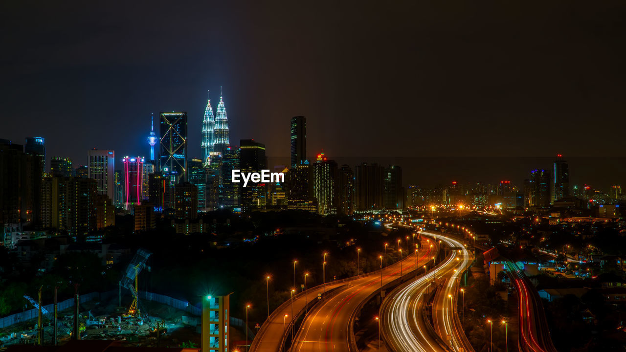 Illuminated modern buildings in city against sky at night