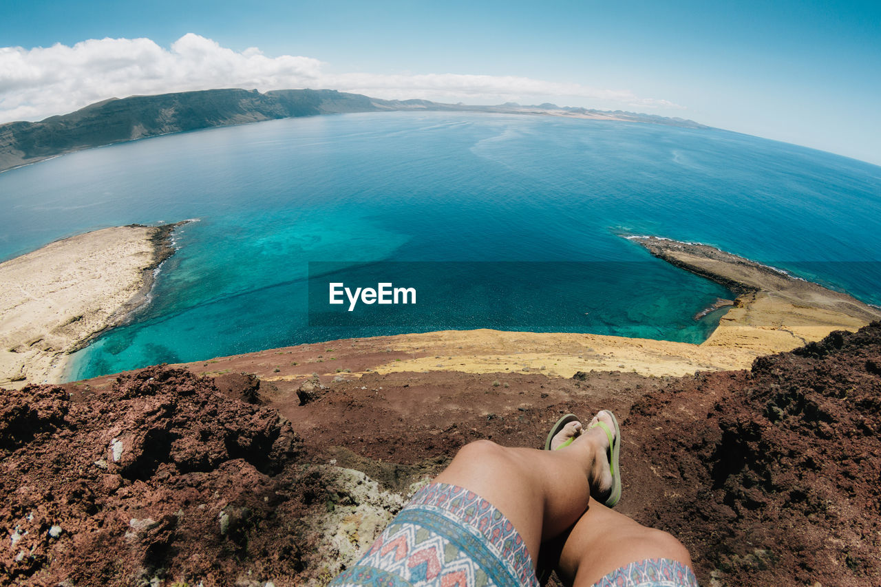 Low section of woman relaxing on rock by sea against sky