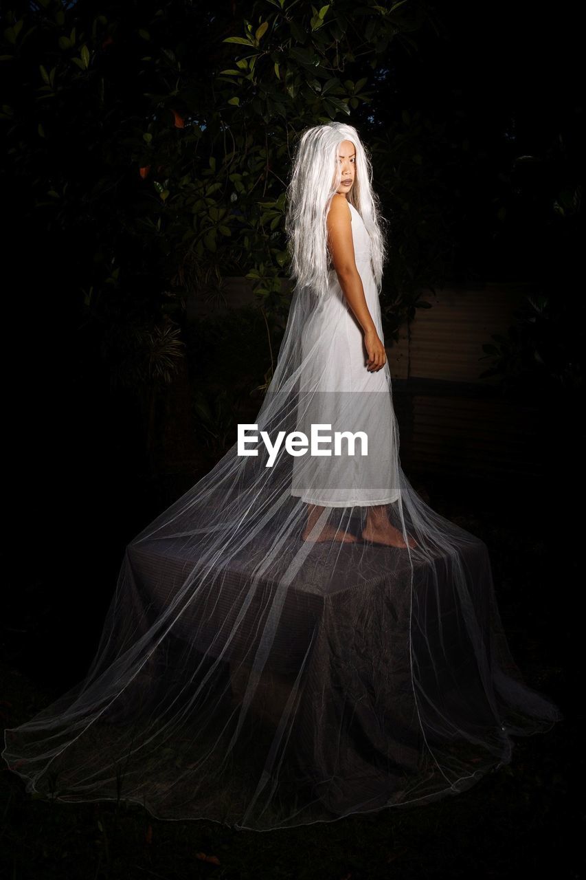 Full length of young woman with long white hair standing against black background