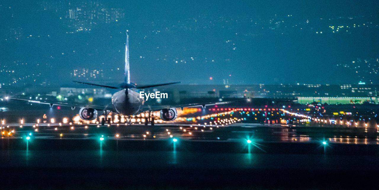 AIRPLANE FLYING OVER ILLUMINATED CITY AGAINST SKY