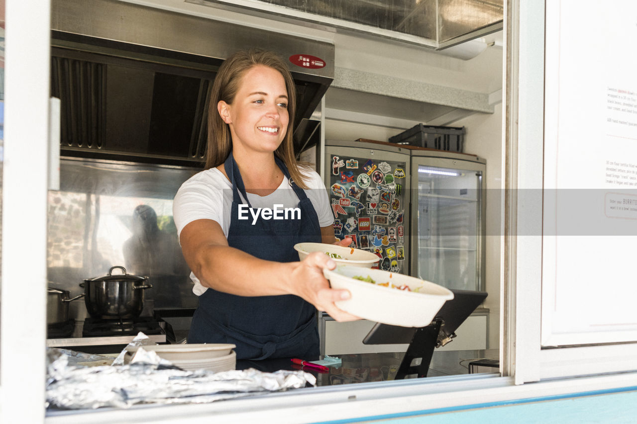 Smiling young female owner giving bowls while standing in food truck
