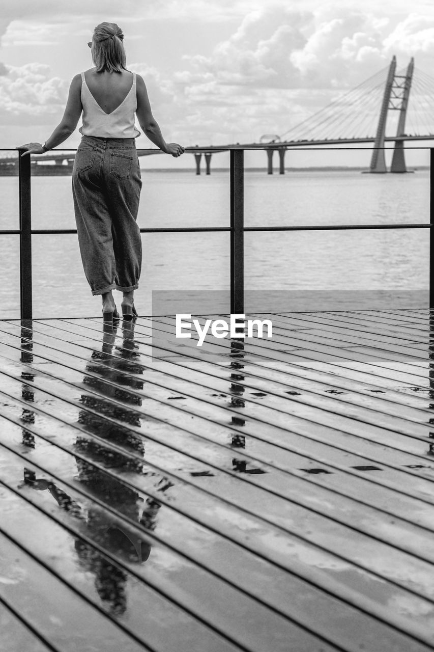 Rear view of woman standing on pier over sea against cloudy sky