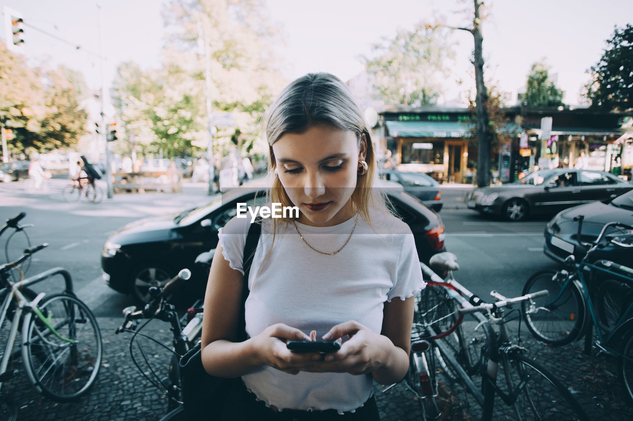 Young woman using mobile phone while standing on sidewalk in city