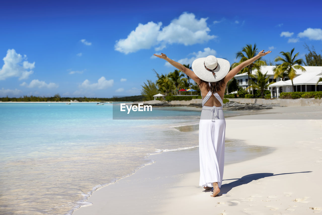 rear view of woman with arms outstretched standing on beach against sky