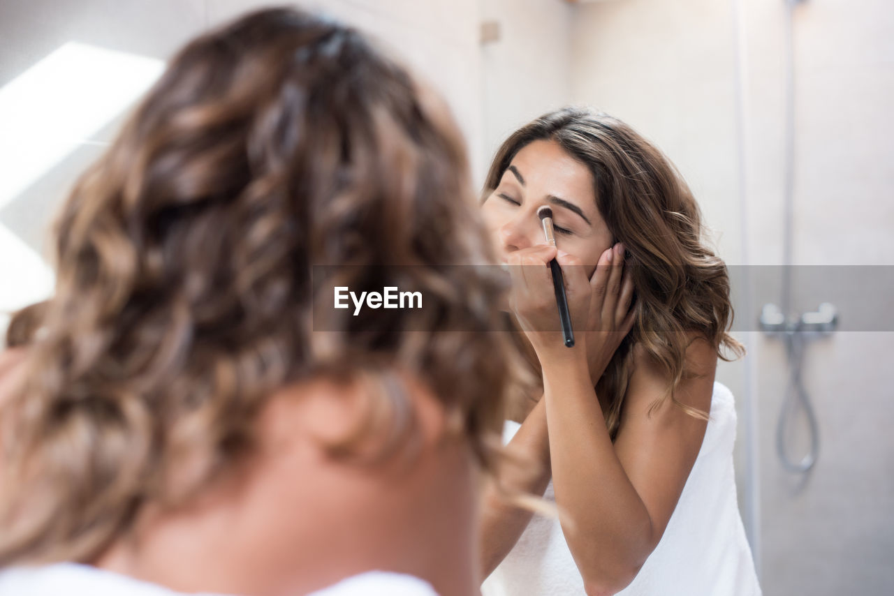 Rear view of women applying make-up standing in bathroom