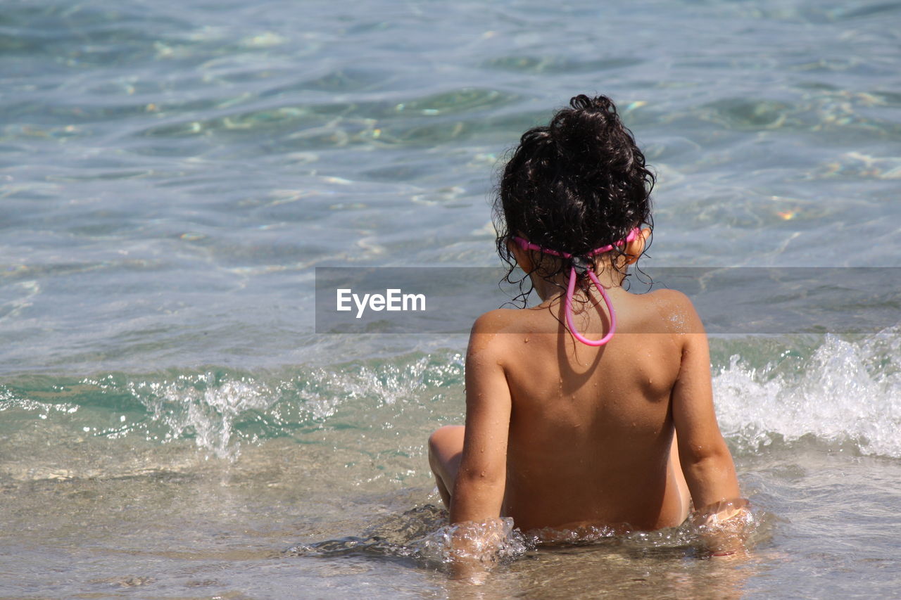 Rear view of shirtless girl sitting in sea