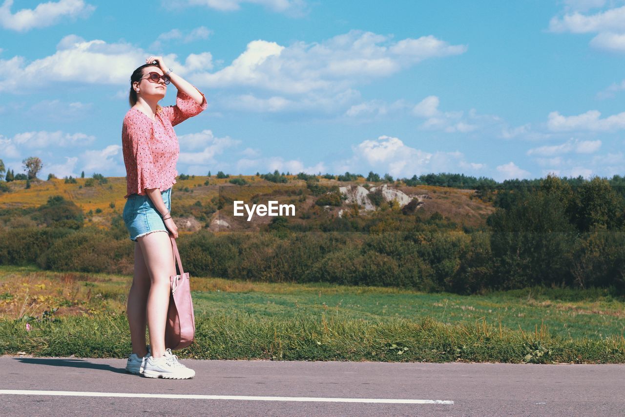 Side view of woman standing on road against sky