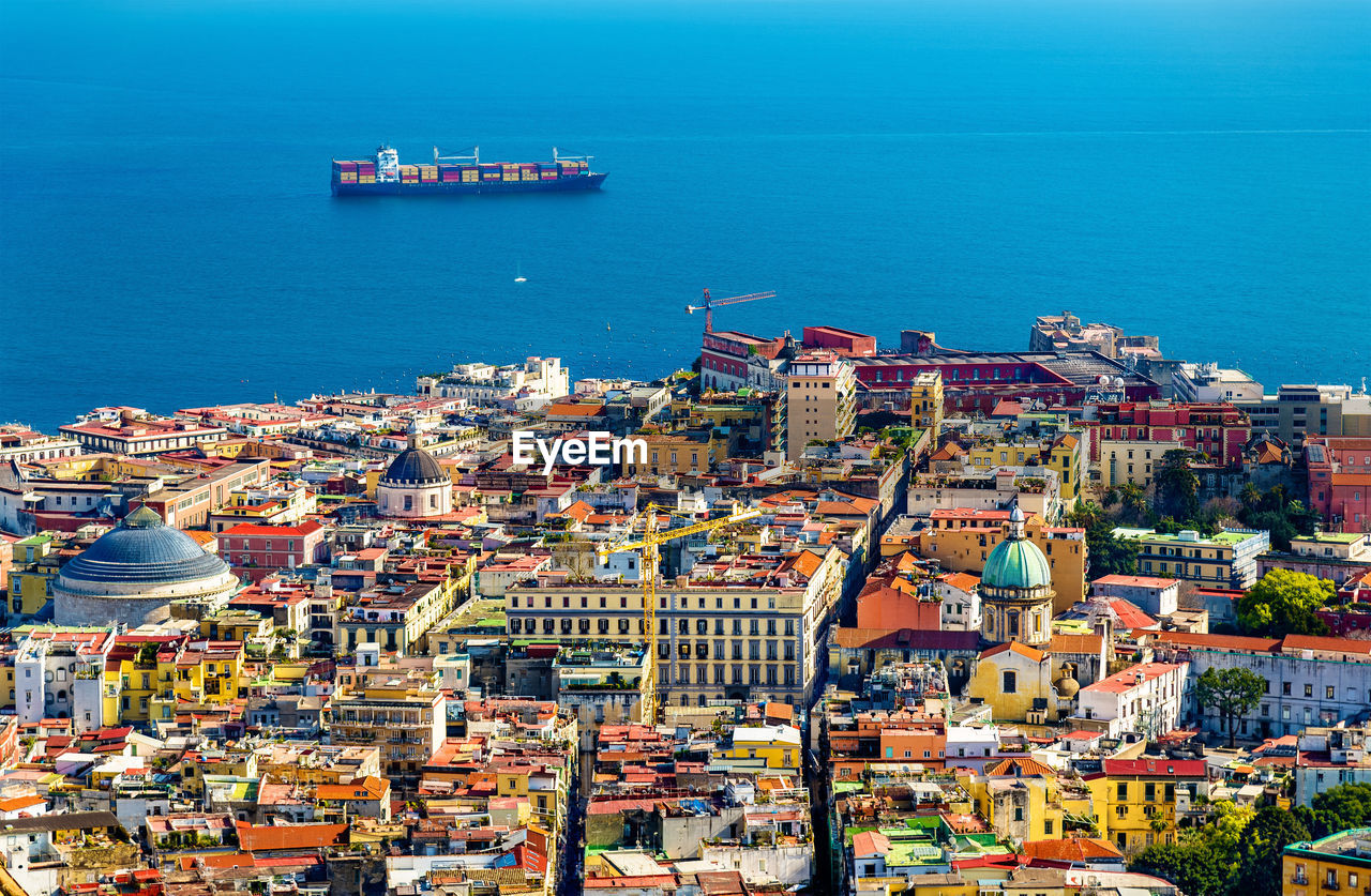 HIGH ANGLE VIEW OF SEA BY BUILDINGS AGAINST SKY