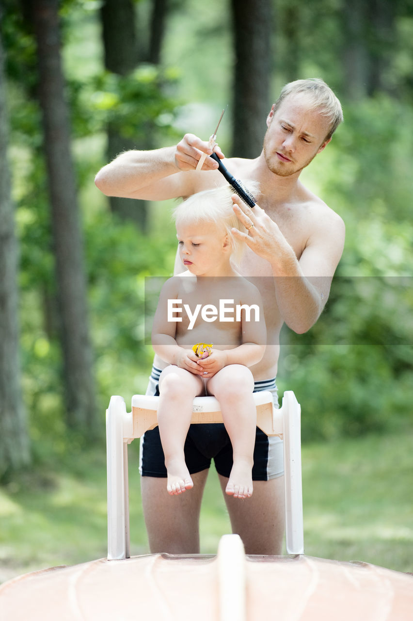 Father cutting hair of son in garden