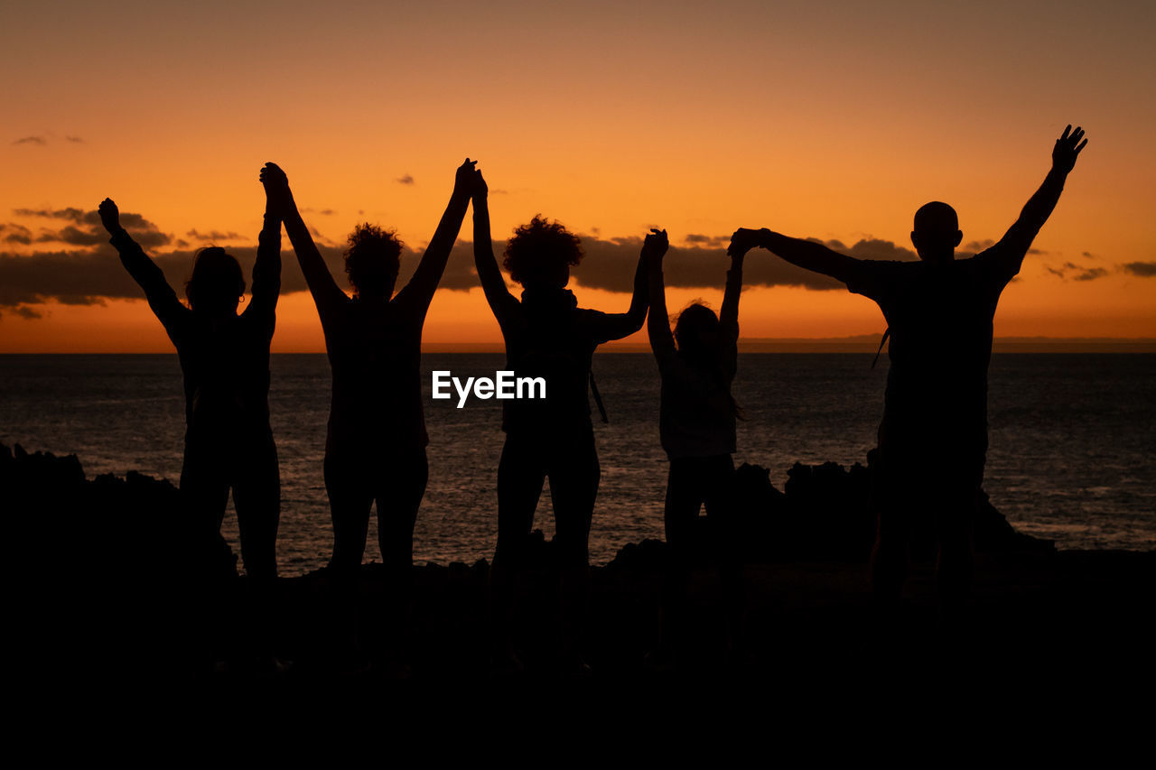 Silhouette of a family hand in hand enjoying a beautiful sunset at the beach. group of friends 