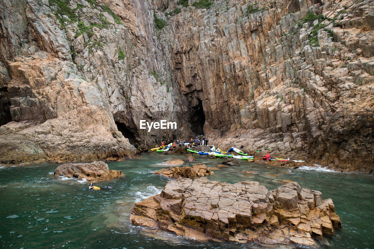 GROUP OF PEOPLE ON ROCKS BY WATER