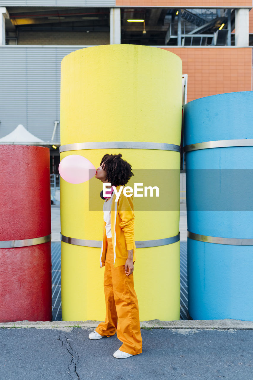 Woman blowing bubblegum in front of multi colored pipes