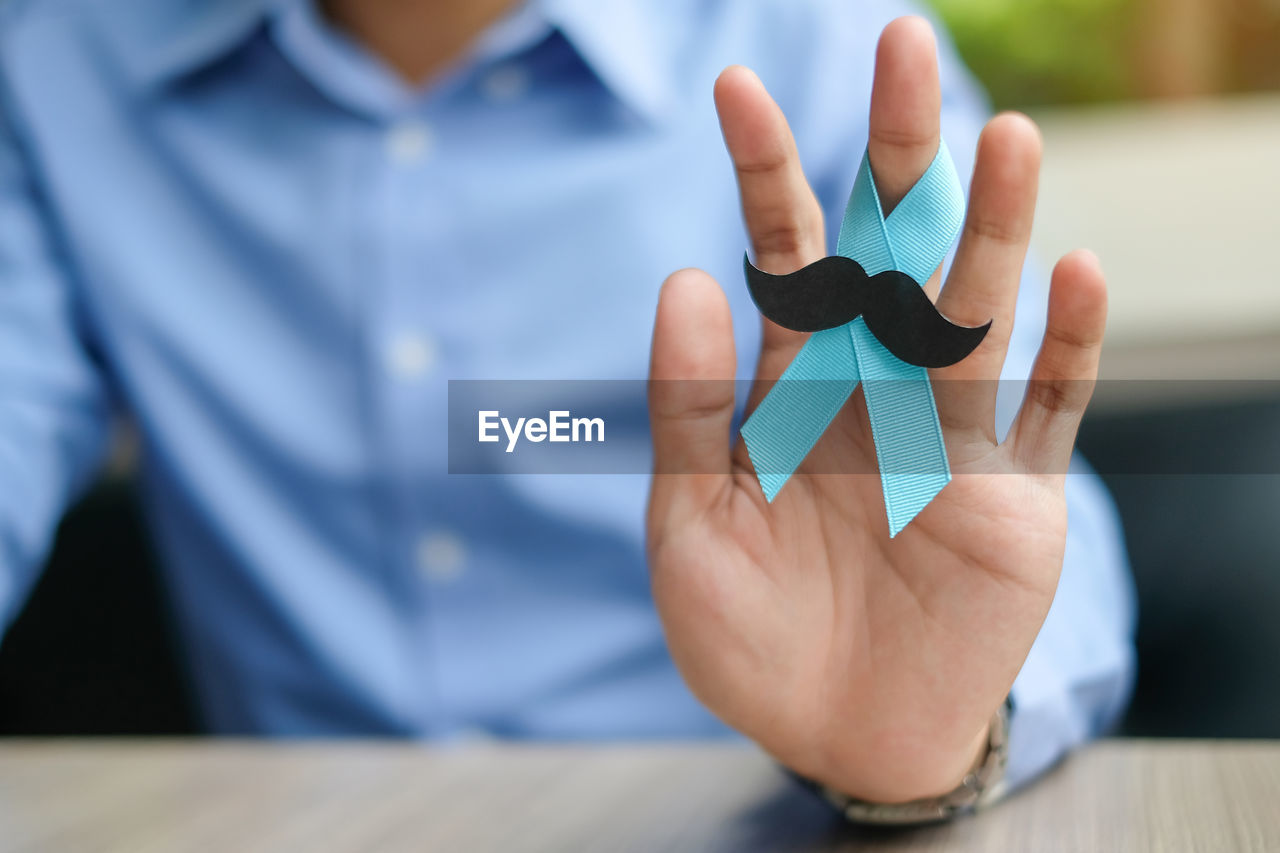 Midsection of man holding blue ribbon with mustache