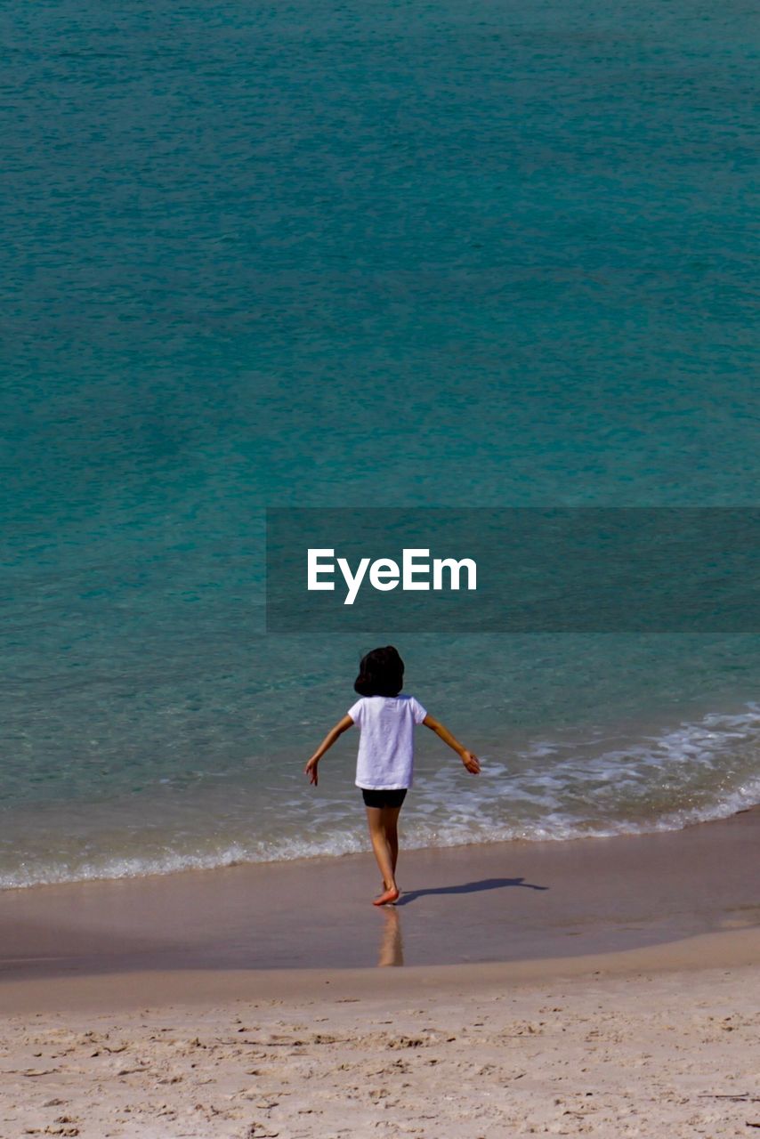 REAR VIEW OF WOMAN STANDING ON BEACH