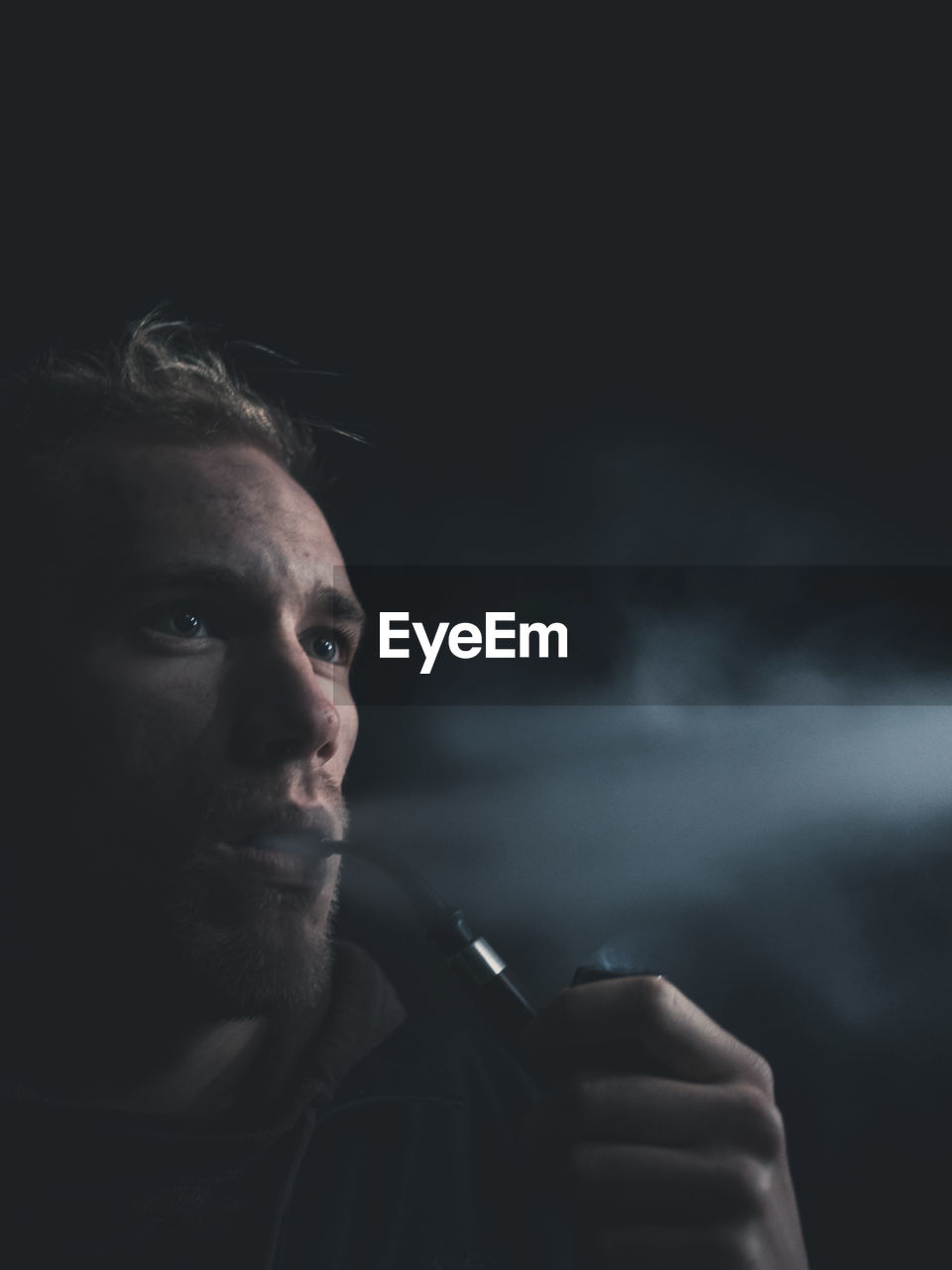 Close-up of young man smoking against black background