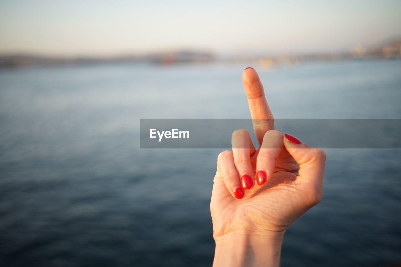 Cropped hand of woman gesturing against sea