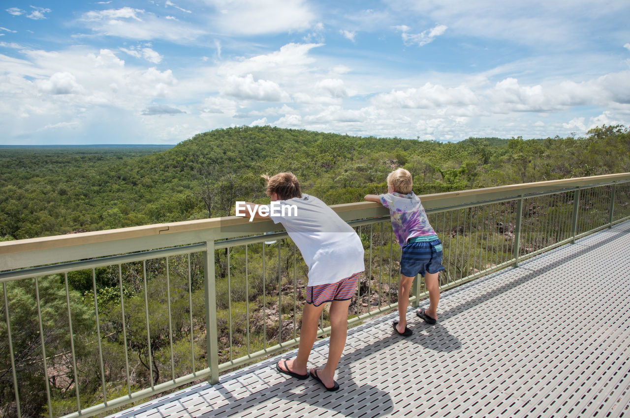 Full length of siblings looking at landscape while standing by railing