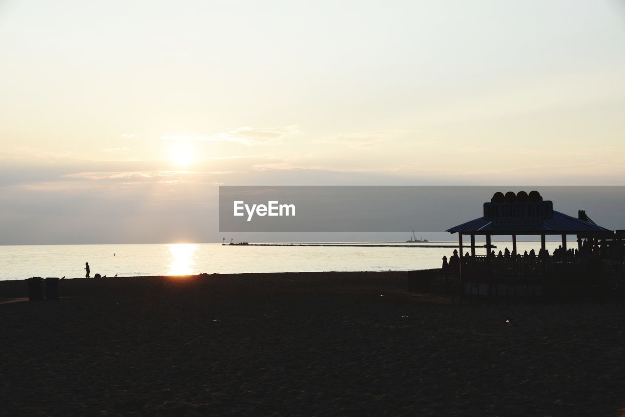 SILHOUETTE BUILT STRUCTURE ON BEACH AGAINST SKY DURING SUNSET