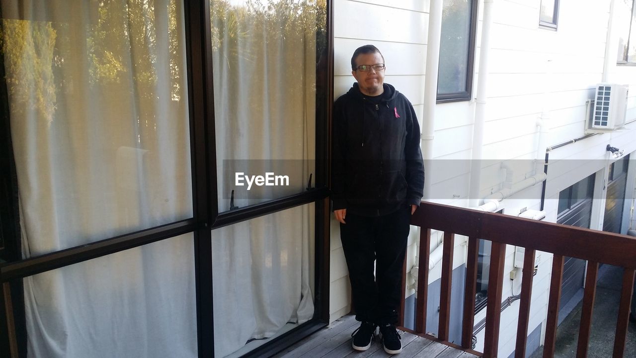 PORTRAIT OF MAN STANDING AGAINST WINDOW