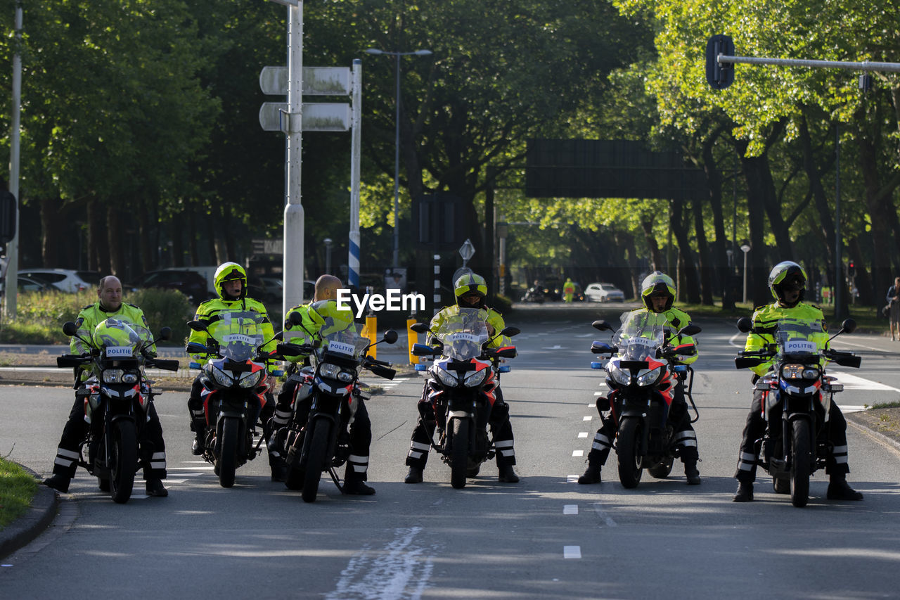 PEOPLE RIDING MOTORCYCLE ON STREET AGAINST TREES