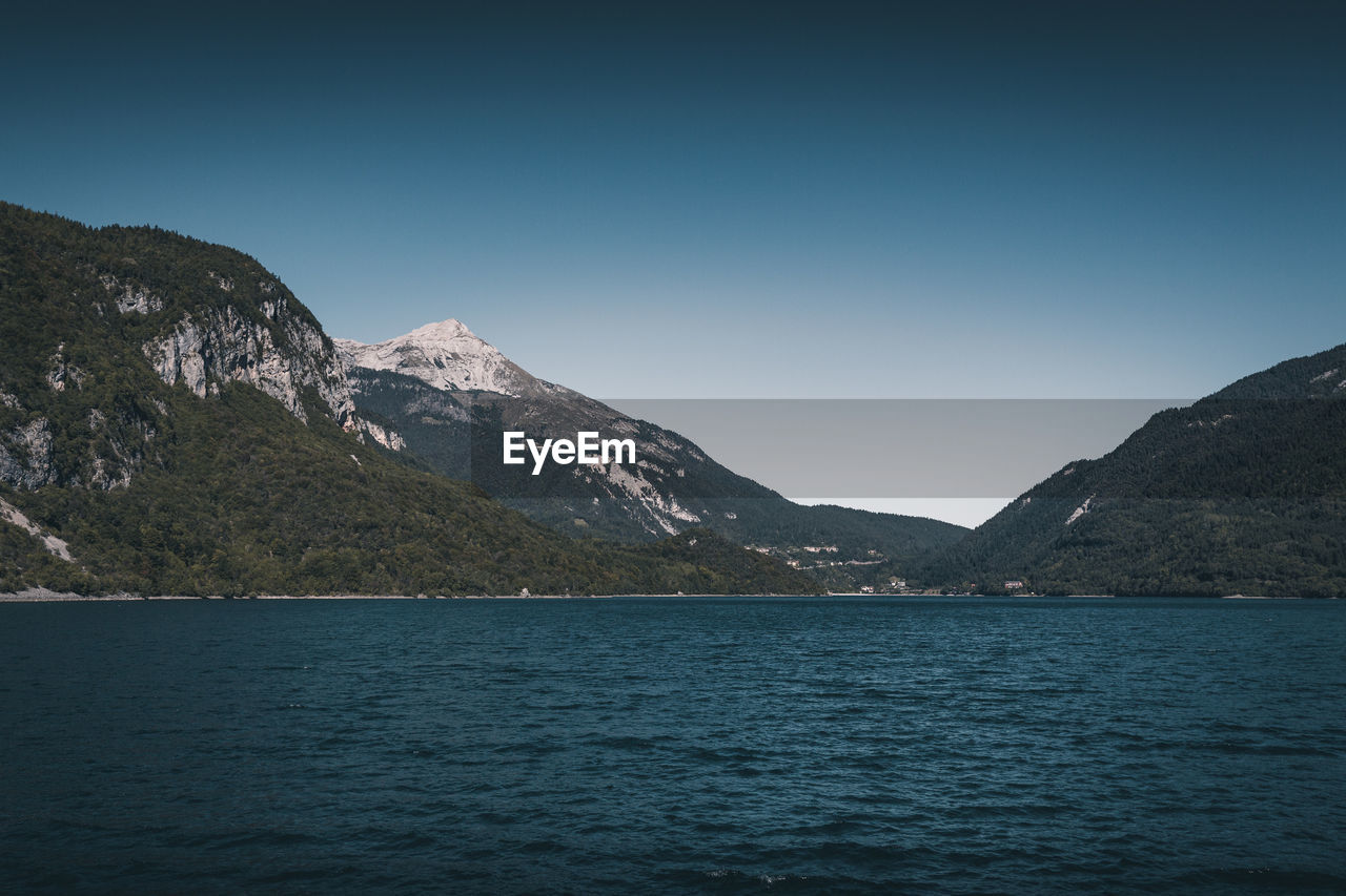 Scenic view of sea and mountains against clear blue sky