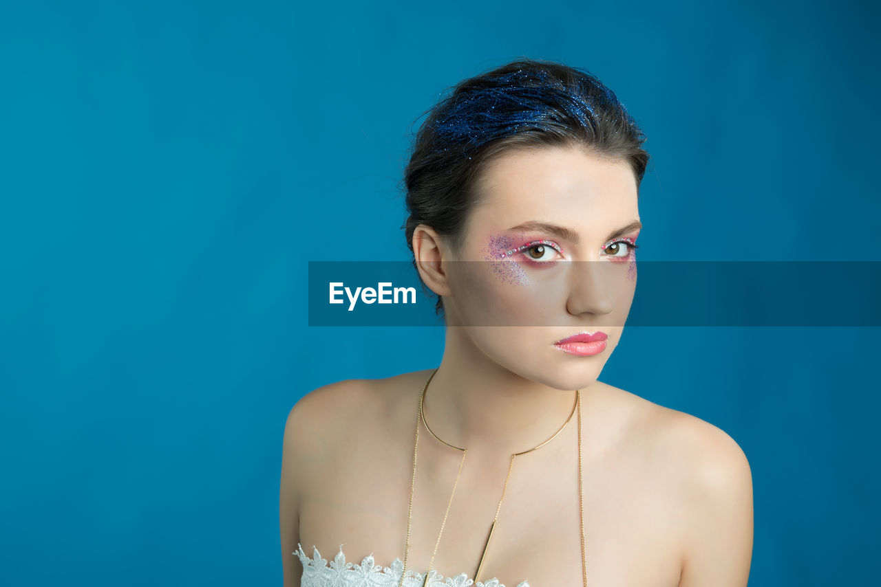 Close-up portrait of young woman against blue background 