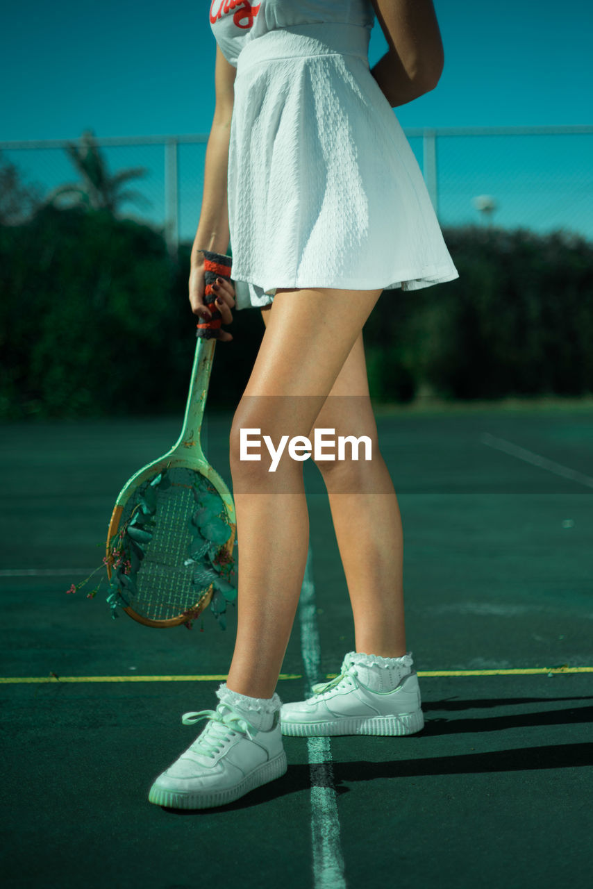 Low section of young woman standing in tennis court