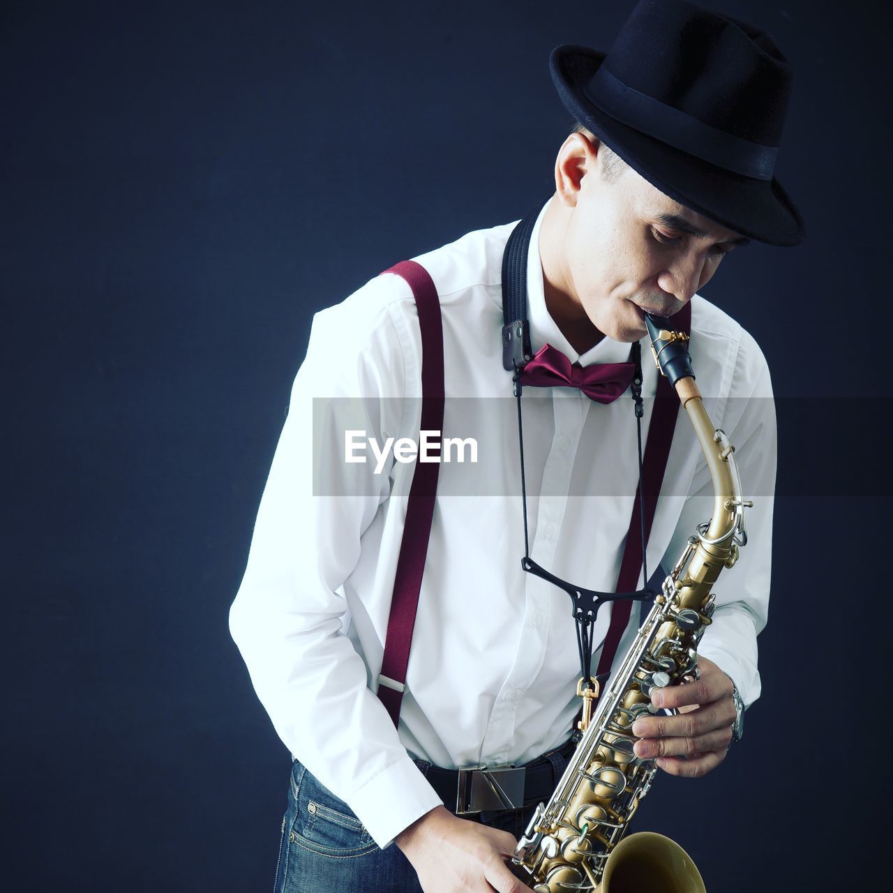 Musician playing saxophone while standing against black background