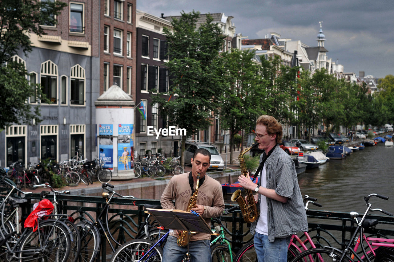 PEOPLE WITH BICYCLE STANDING ON CITY IN BACKGROUND