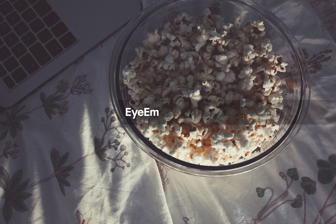 High angle view of popcorn in bowl by laptop on bed