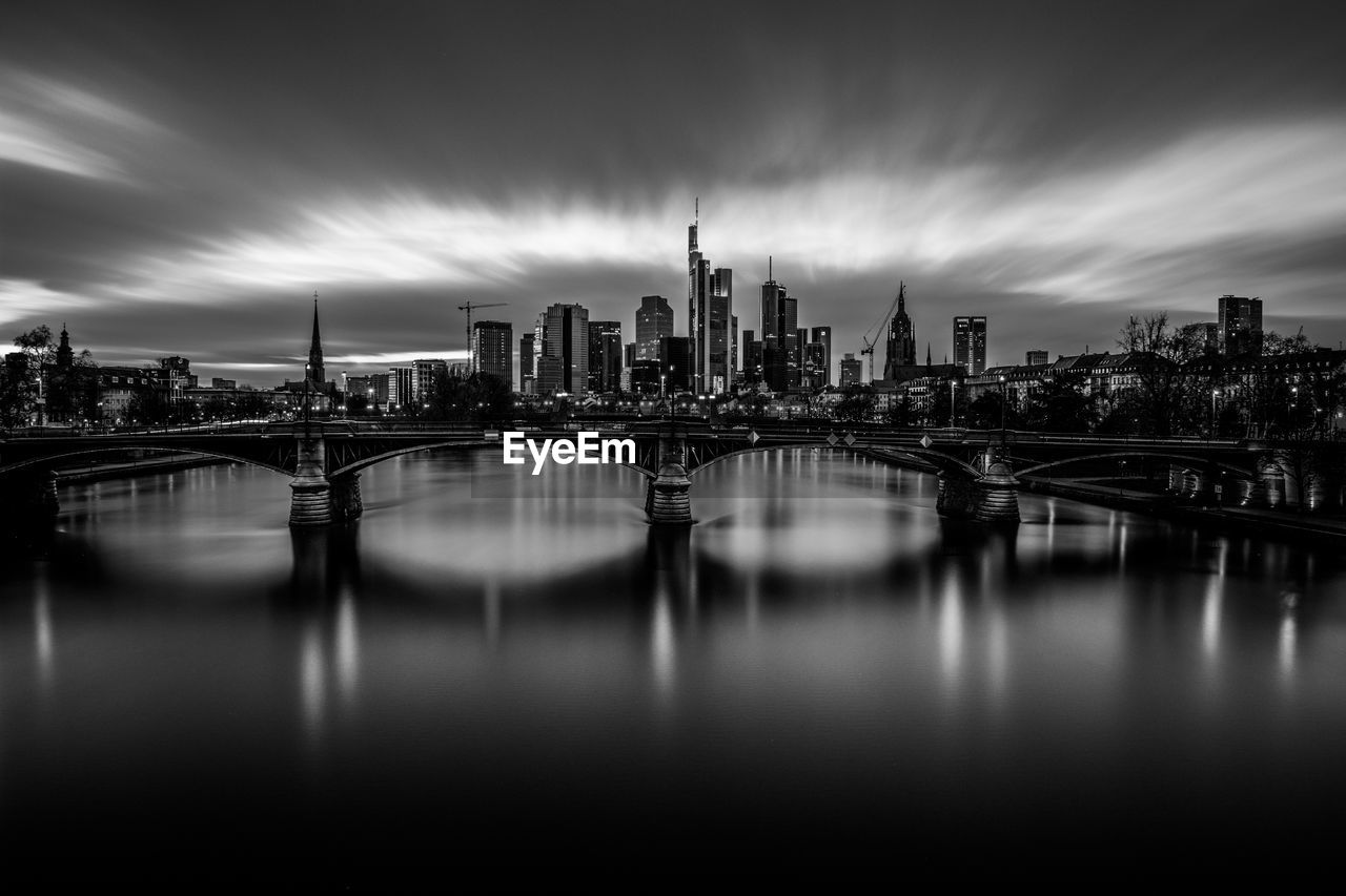 Bridge over river by buildings in city against sky in frankfurt, germany 