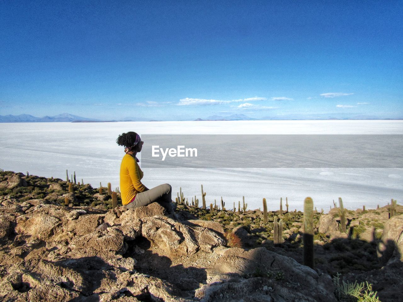 Woman sitting on rock looking at a salt flat against a blue sky