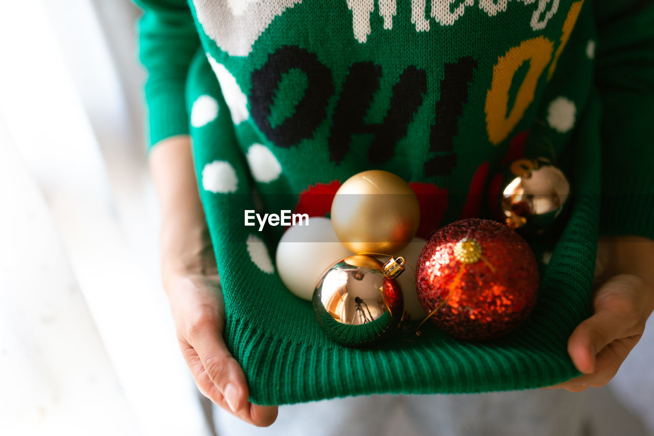 Midsection of woman carrying christmas ornament in sweater