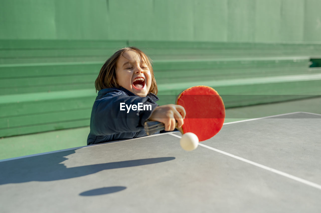 Cheerful boy playing table tennis on sunny day