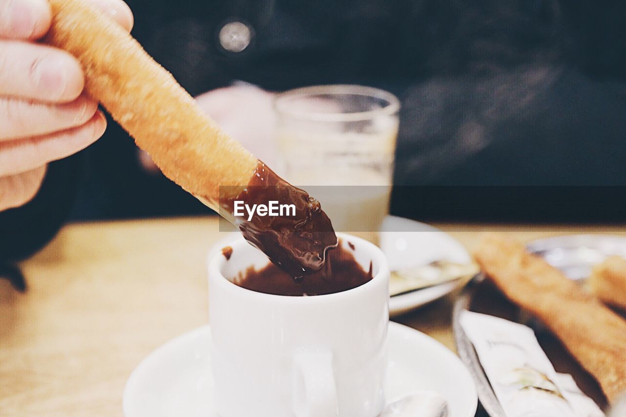 Cropped image of person dipping churro in chocolate at table