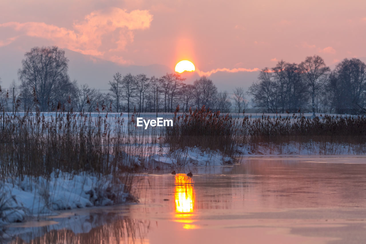 SCENIC VIEW OF FROZEN LAKE AGAINST ORANGE SKY DURING WINTER