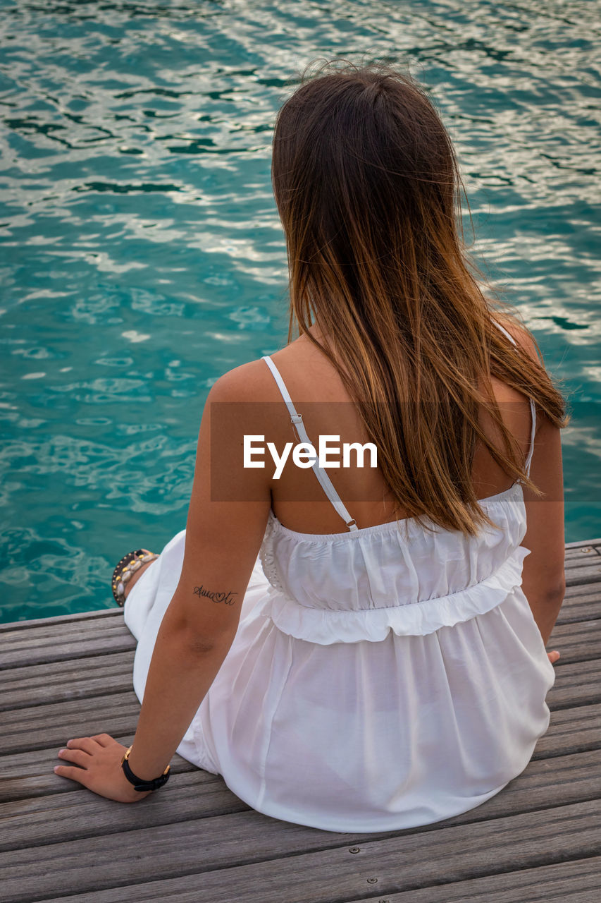 Rear view of woman sitting at swimming pool