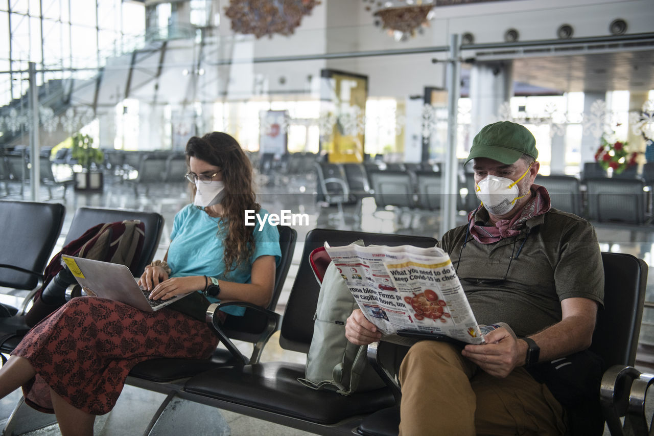 Middle aged man and a young woman wear face masks due to the coronavirus epidemic while waiting at a deserted airport in khajuraho, madhya pradesh, india.