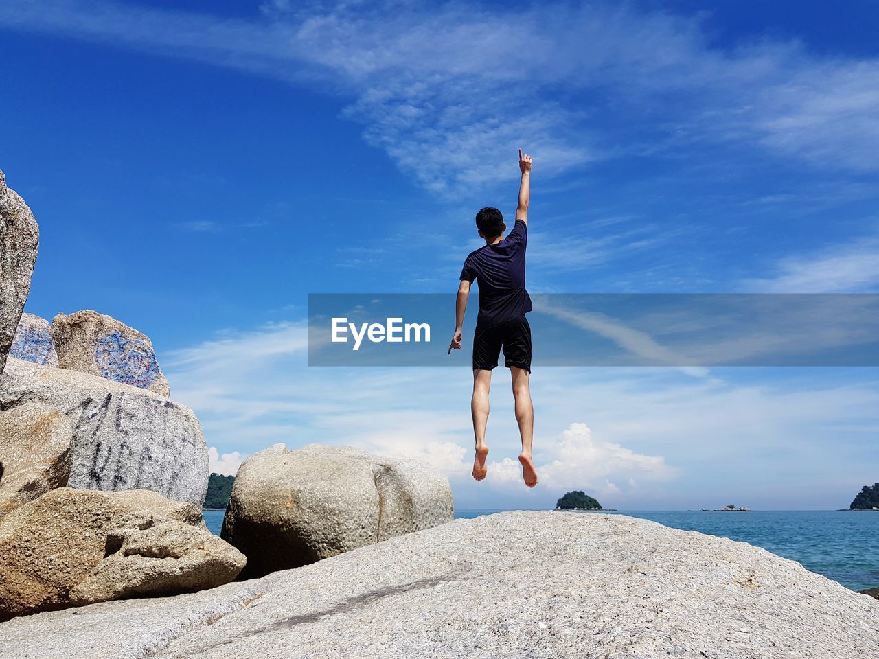 Rear view of man jumping on rock against sea