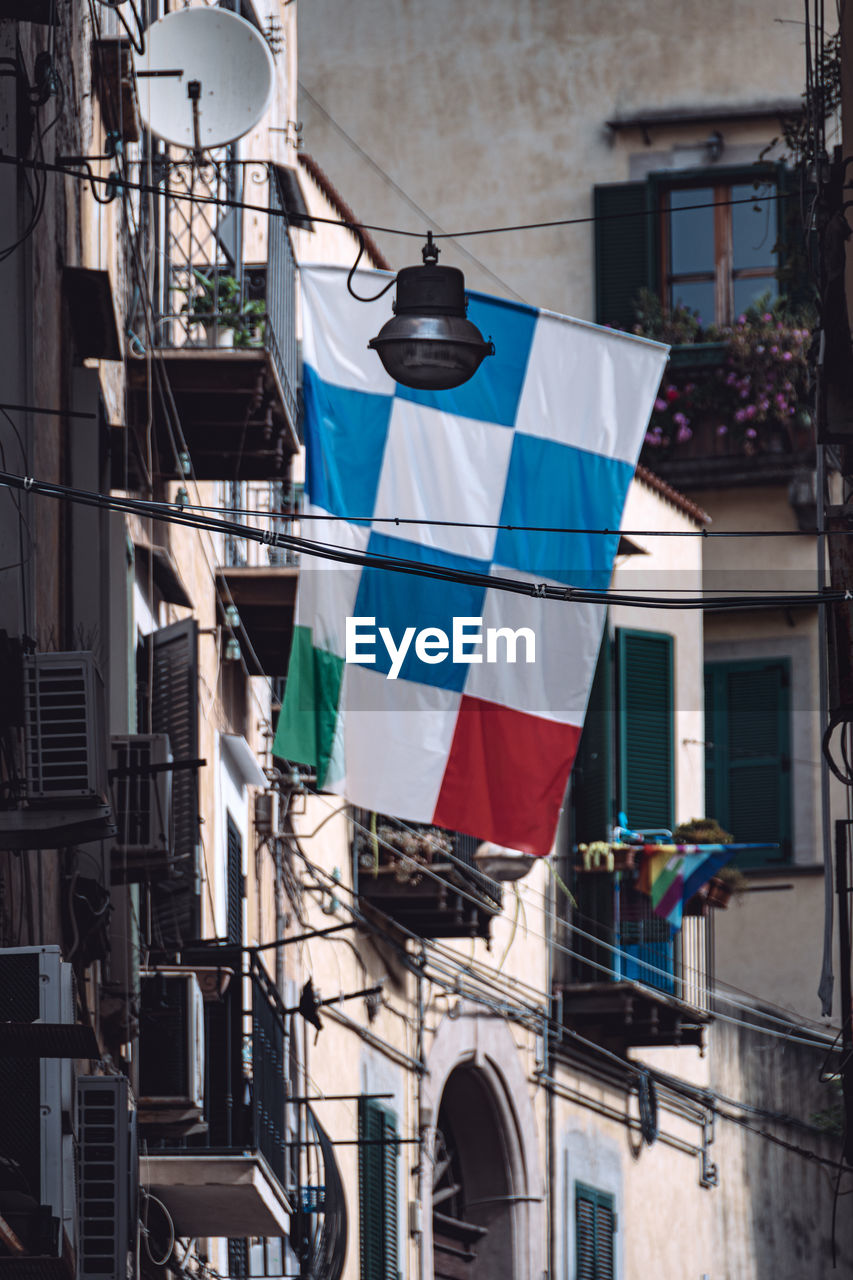 architecture, building exterior, urban area, built structure, blue, street, road, city, building, no people, flag, art, day, low angle view, hanging, residential district, nature, window, facade, outdoors, downtown, drying, clothesline, patriotism, sunlight