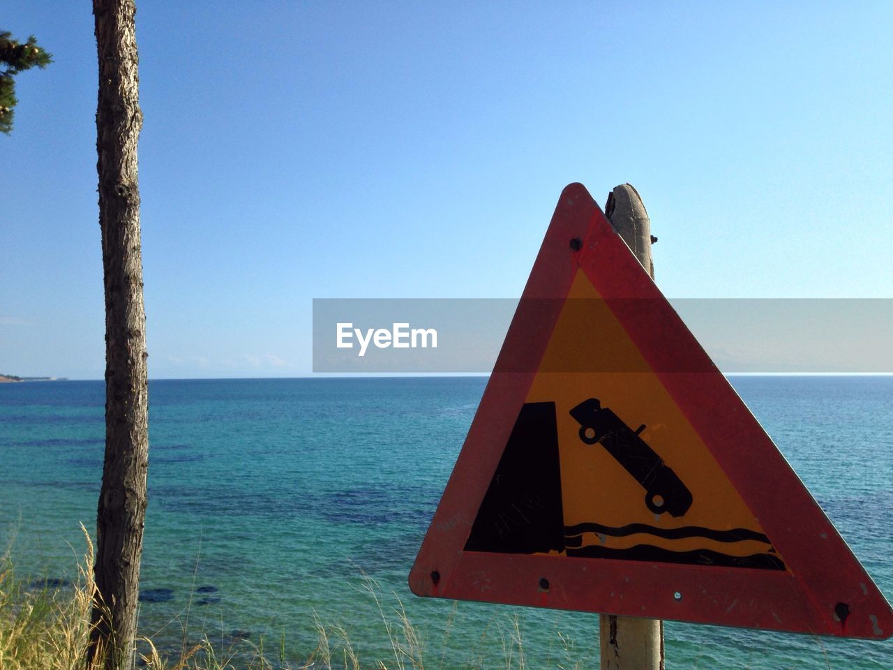 Close-up of road sign against sea and clear sky on sunny day