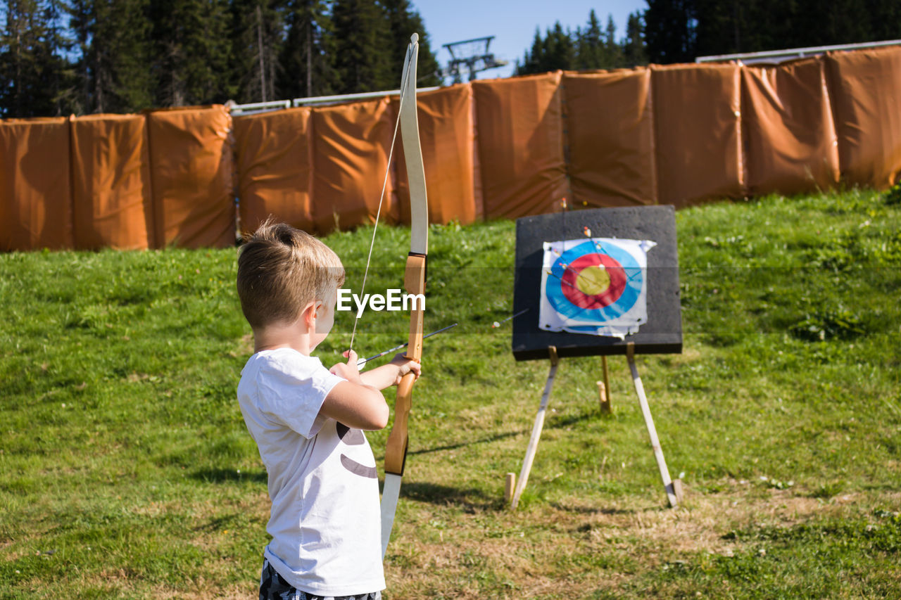 Boy using bow and arrow and shooting at the target outdoors.