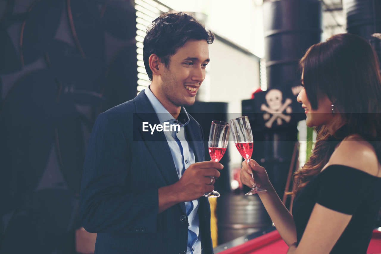 Smiling couple toasting red wineglasses while standing in bar