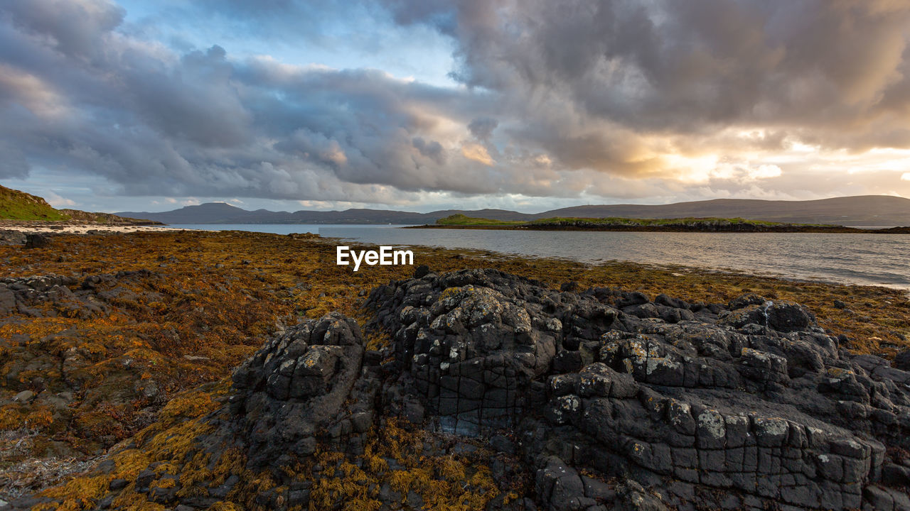 SCENIC VIEW OF ROCKS ON SHORE AGAINST SKY DURING SUNSET