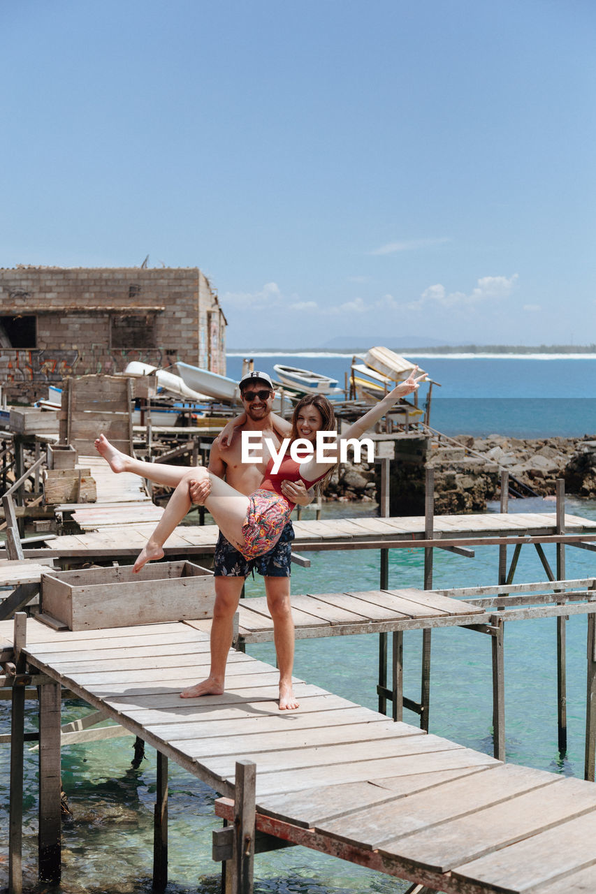 Man carrying woman on pier over sea