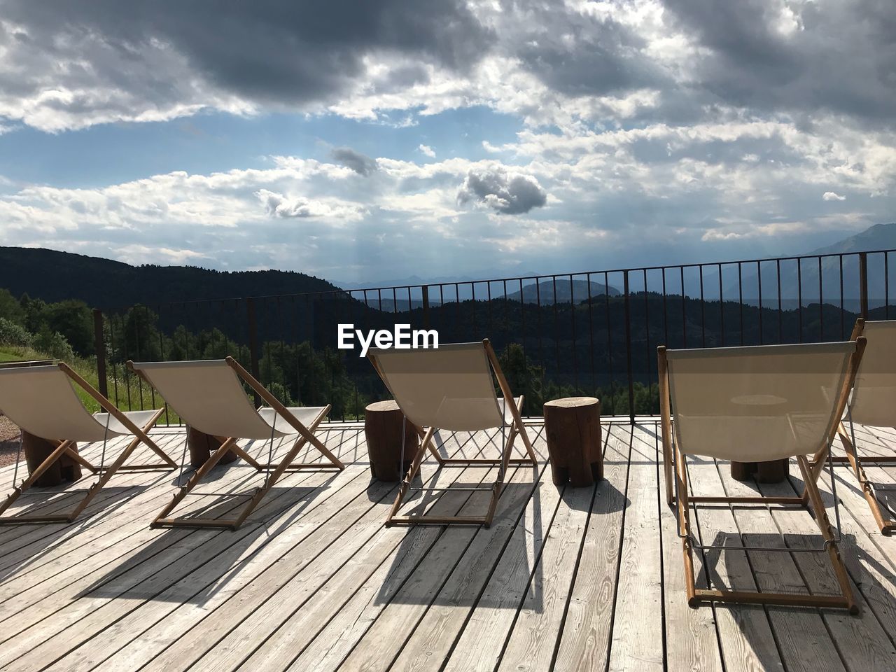 Empty chairs on deck chair by sea against sky