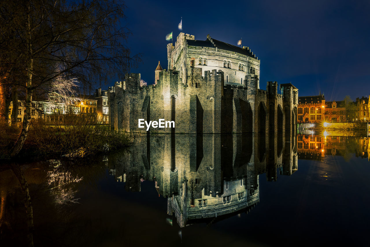 ILLUMINATED BUILDINGS BY RIVER AT NIGHT