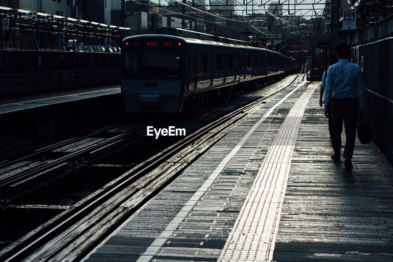 REAR VIEW OF MAN STANDING ON RAILROAD TRACK