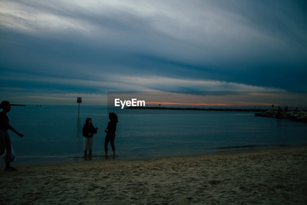 Silhouette people standing on beach against sky