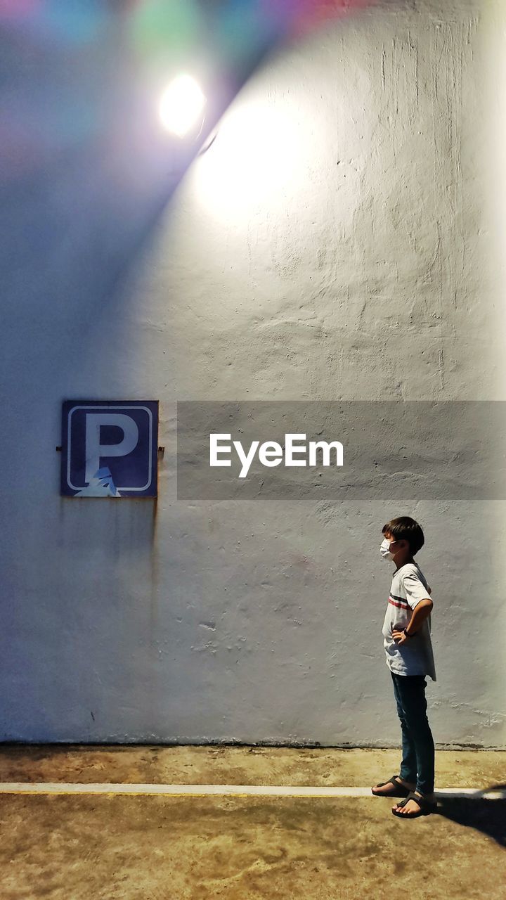 Full length of kid with face mask standing against wall